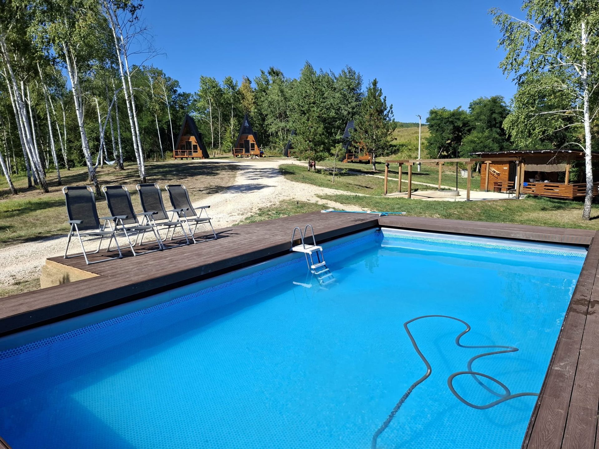 Pool mit Holzdeck, Liegestühlen und Tiny-Häusern